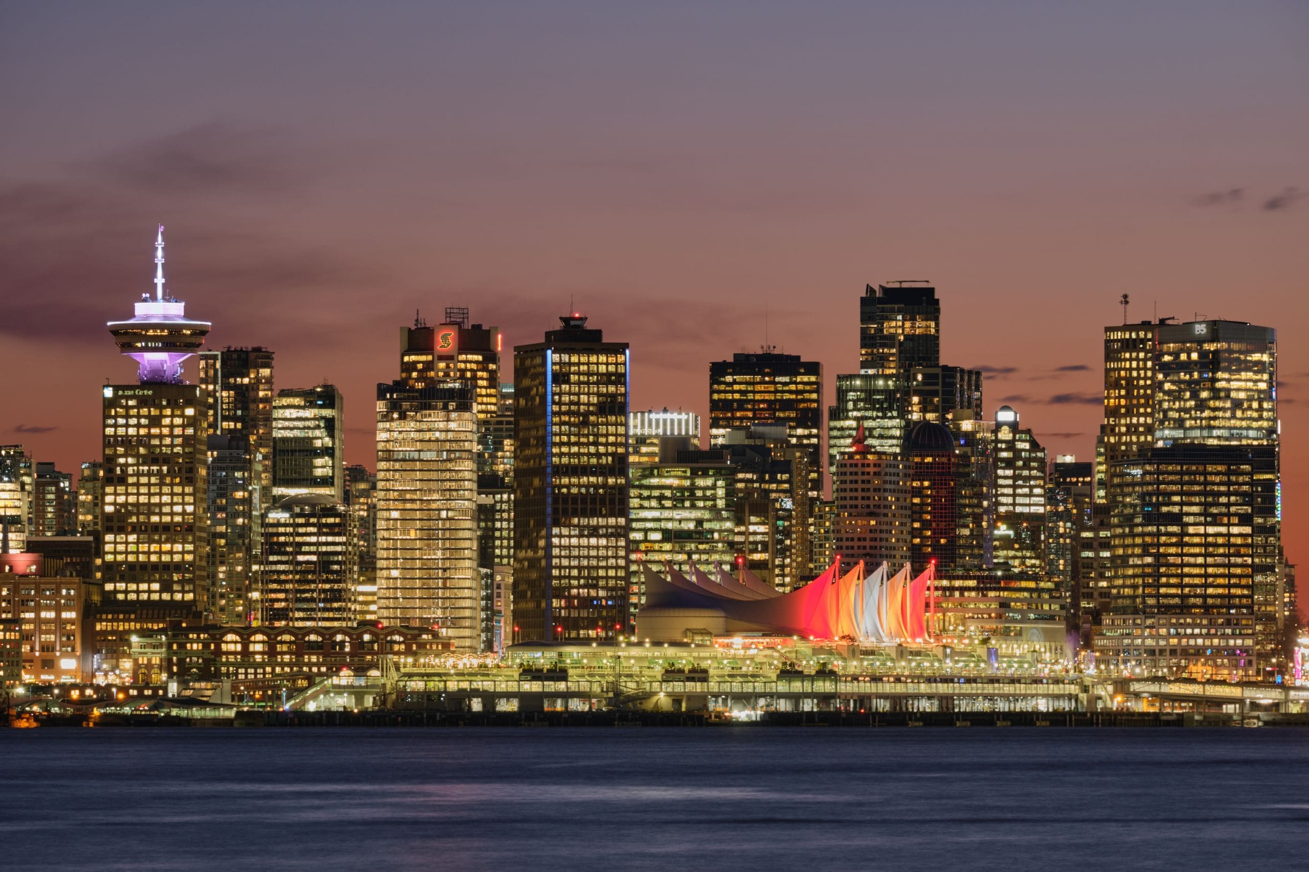 Vancouver's harbour skyline at dusk, glass towers glowing beneath the North Shore mountains